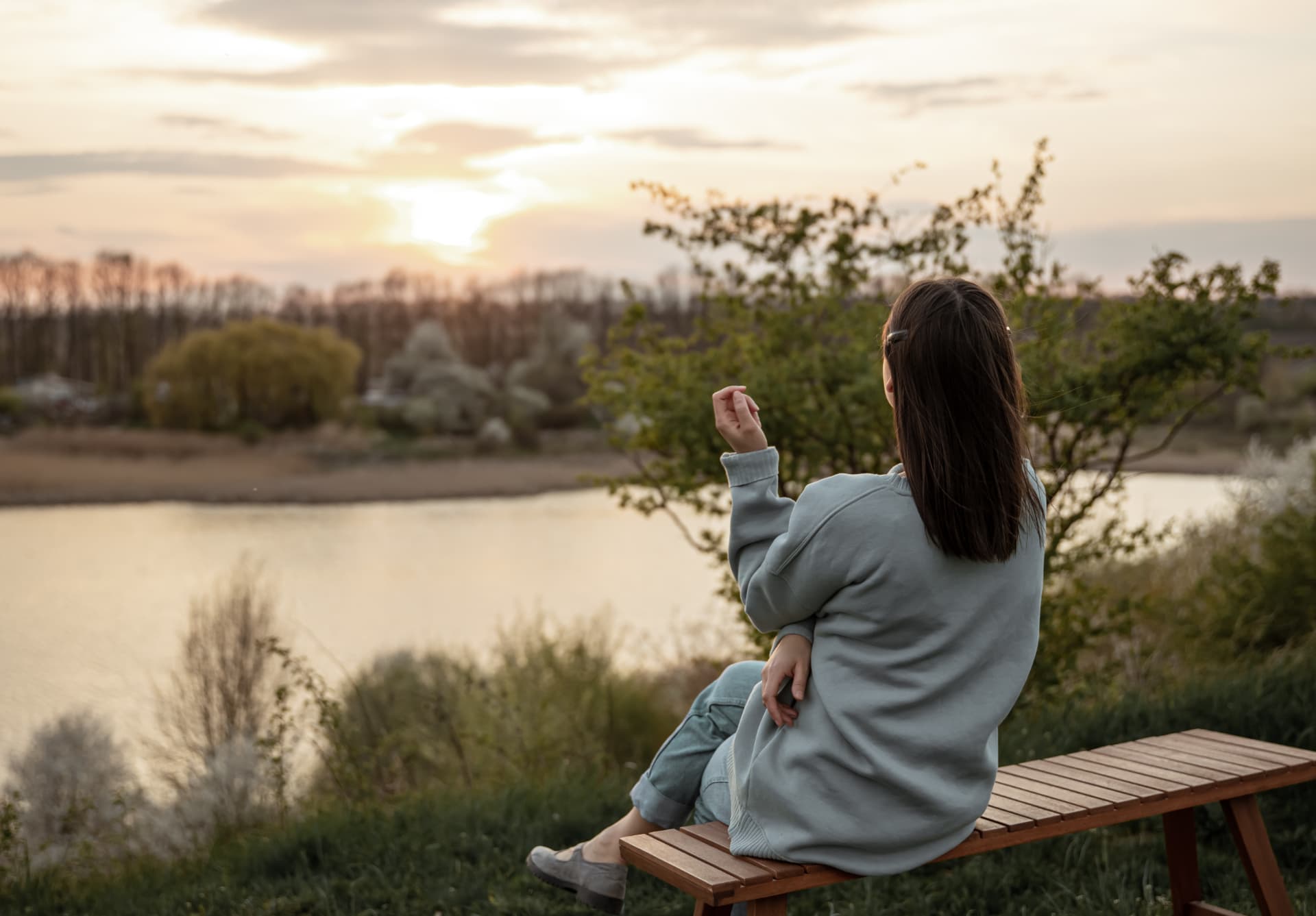 Frau auf einer Bank am Fluss im Sonnenuntergang